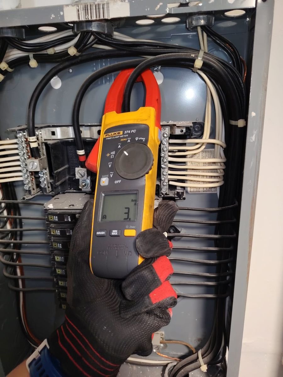 Técnico midiendo corriente con amperímetro de gancho en un tablero eléctrico